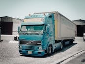 A blue Volvo truck parked outside a warehouse in an industrial area, daytime scene.